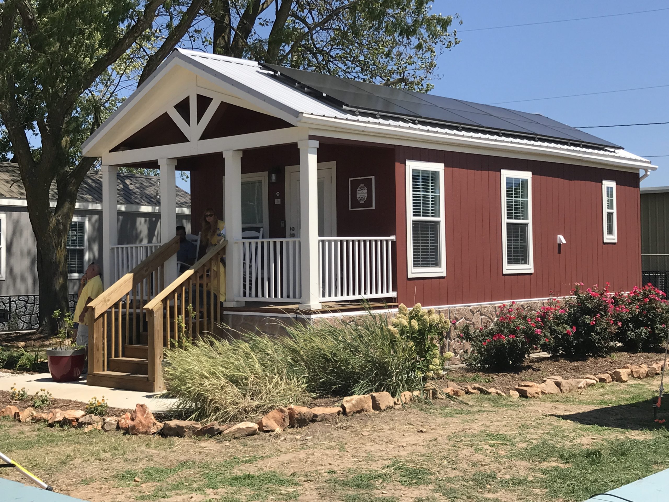 A small, red house at Eden Village in Springfield, MO with white trim and solar panels mounted to its aluminum roof.