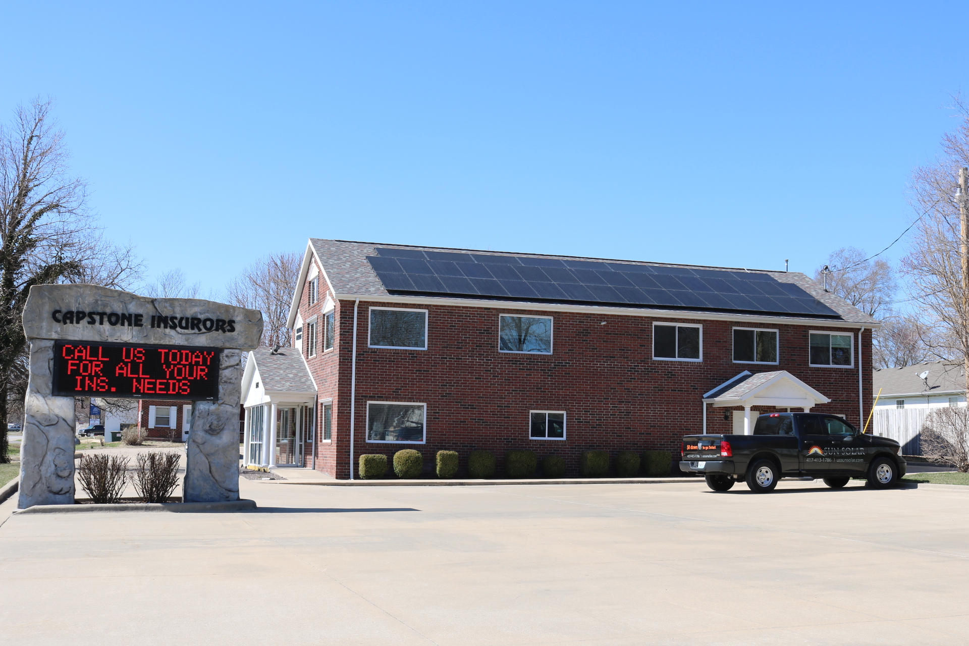 The Capstone Insurors building in Bolivar, MO with an array of solar panels on the roof and a black truck from Sun Solar in the parking lot.