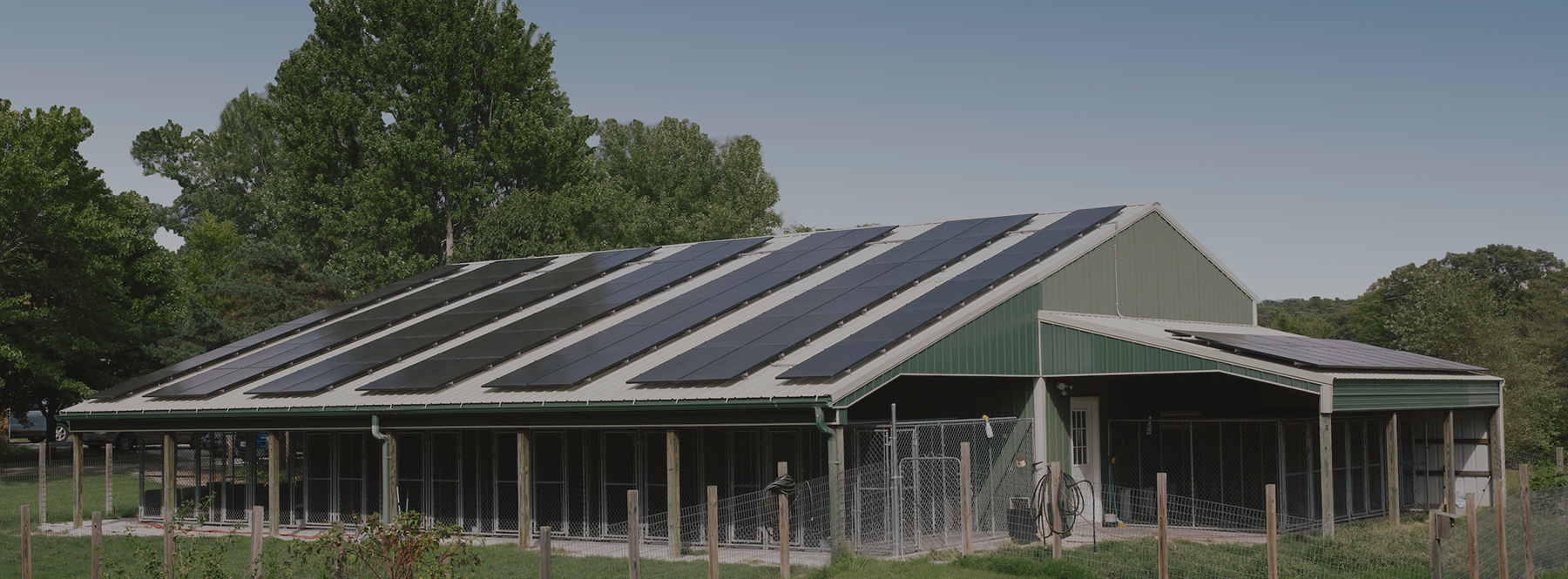 A large, green steel building with a large array of roof-mounted solar panels.