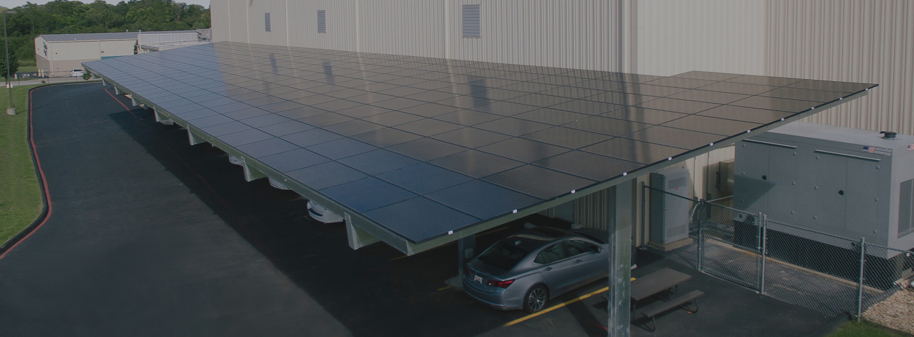Large, metal carport with solar panels mounted to the roof next to a large, tan aluminum building.