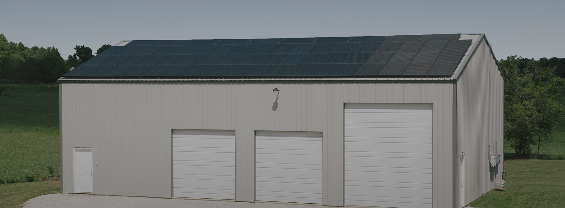 Grey, aluminum building with 3 white garage doors and roof-mounted solar panels.