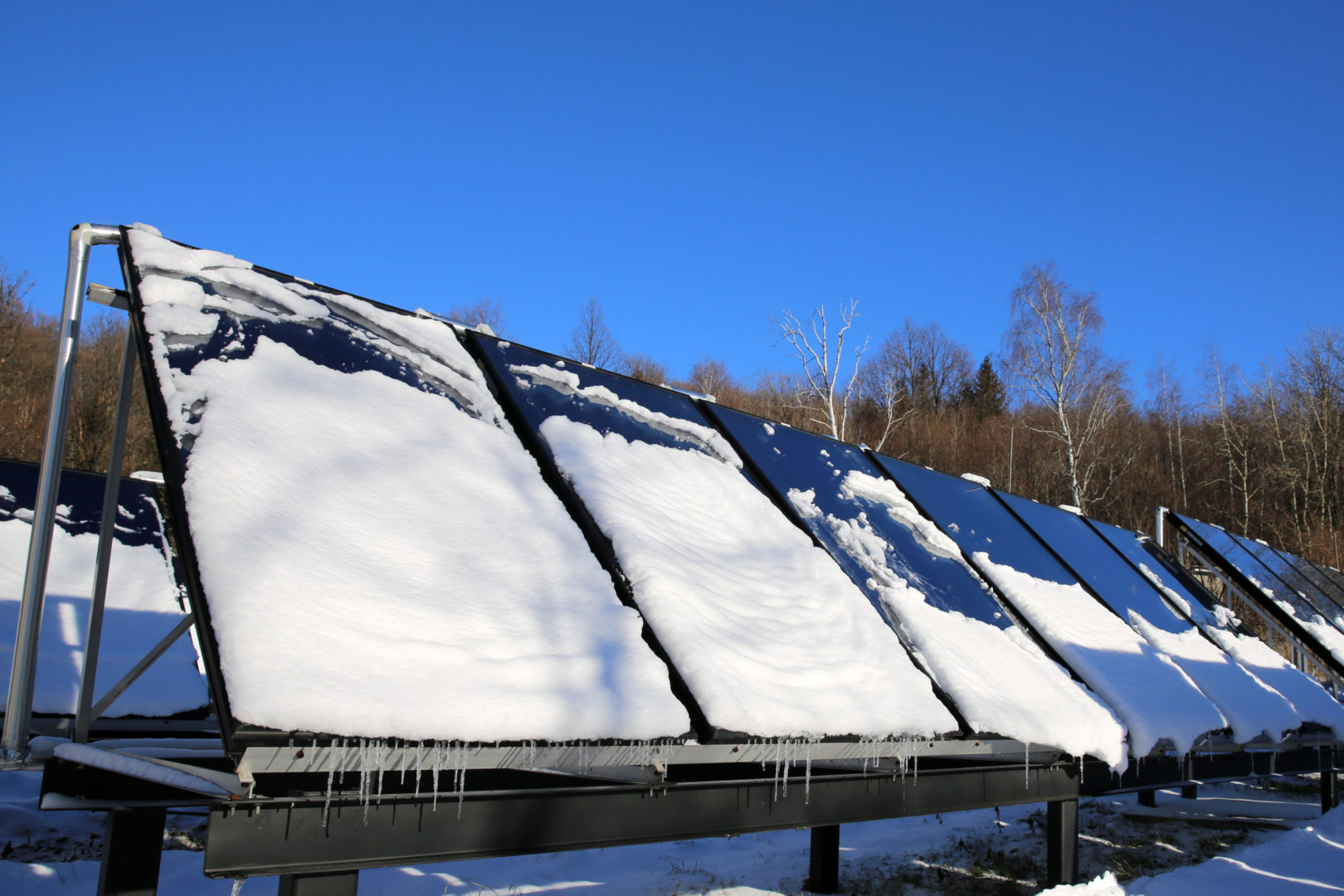An array of ground-mounted solar panels with snow partially covering it.