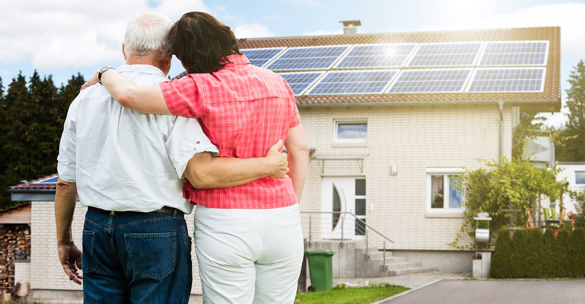 A happy older couple stands on their driveway and views their newly financed, roof-mounted solar project.