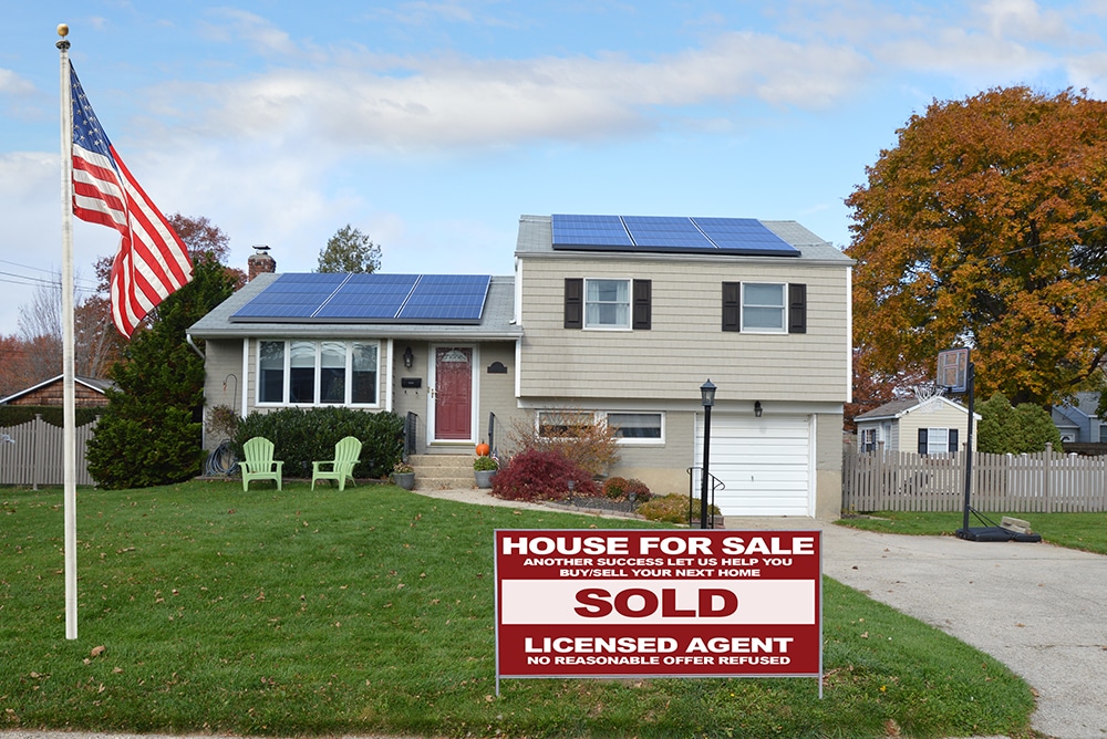 Home with solar on the roof and an American Flag and for sale sign in the front yard